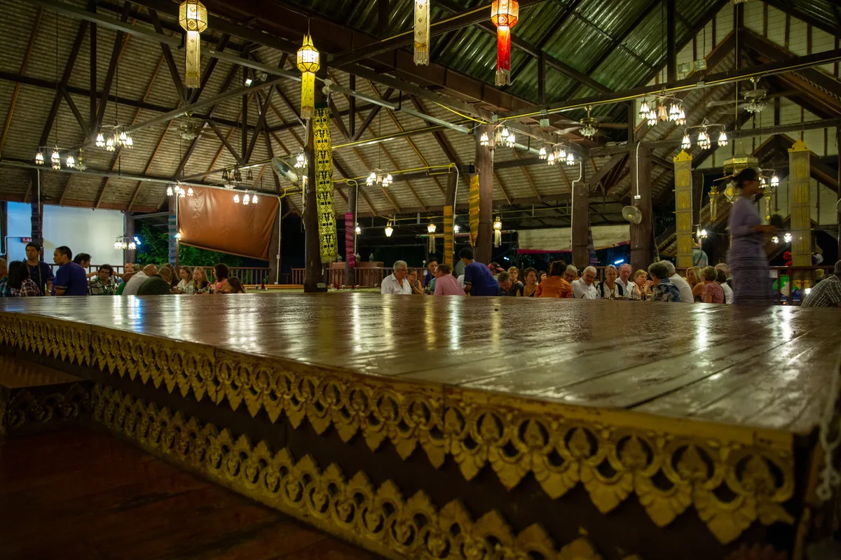 The open teak pavilion of a Khantoke dinner hall in Chiang Mai, strung with lanterns